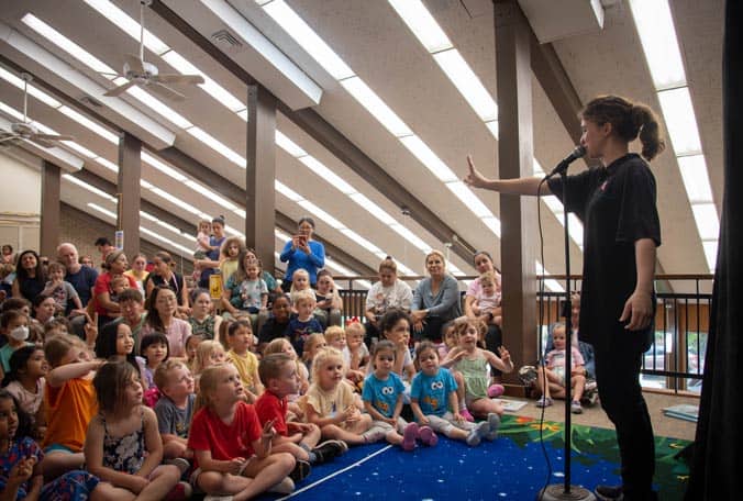 Woman on stage in front of group of kids for Summer Reading Puppet Theatre