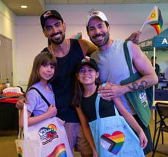 Two men with two girls wearing pride hats and bags